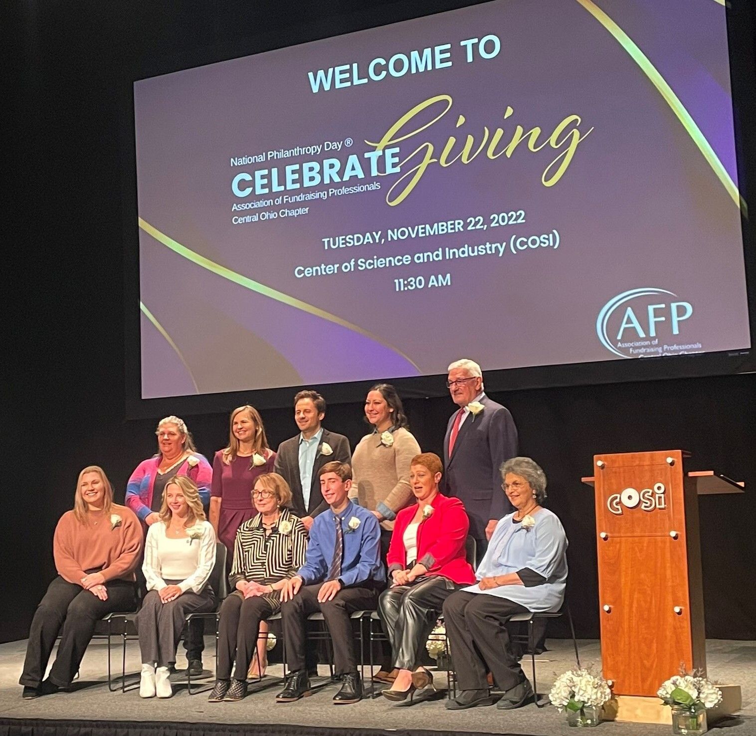 A group of 11 award winners pose on stage for a photograph.