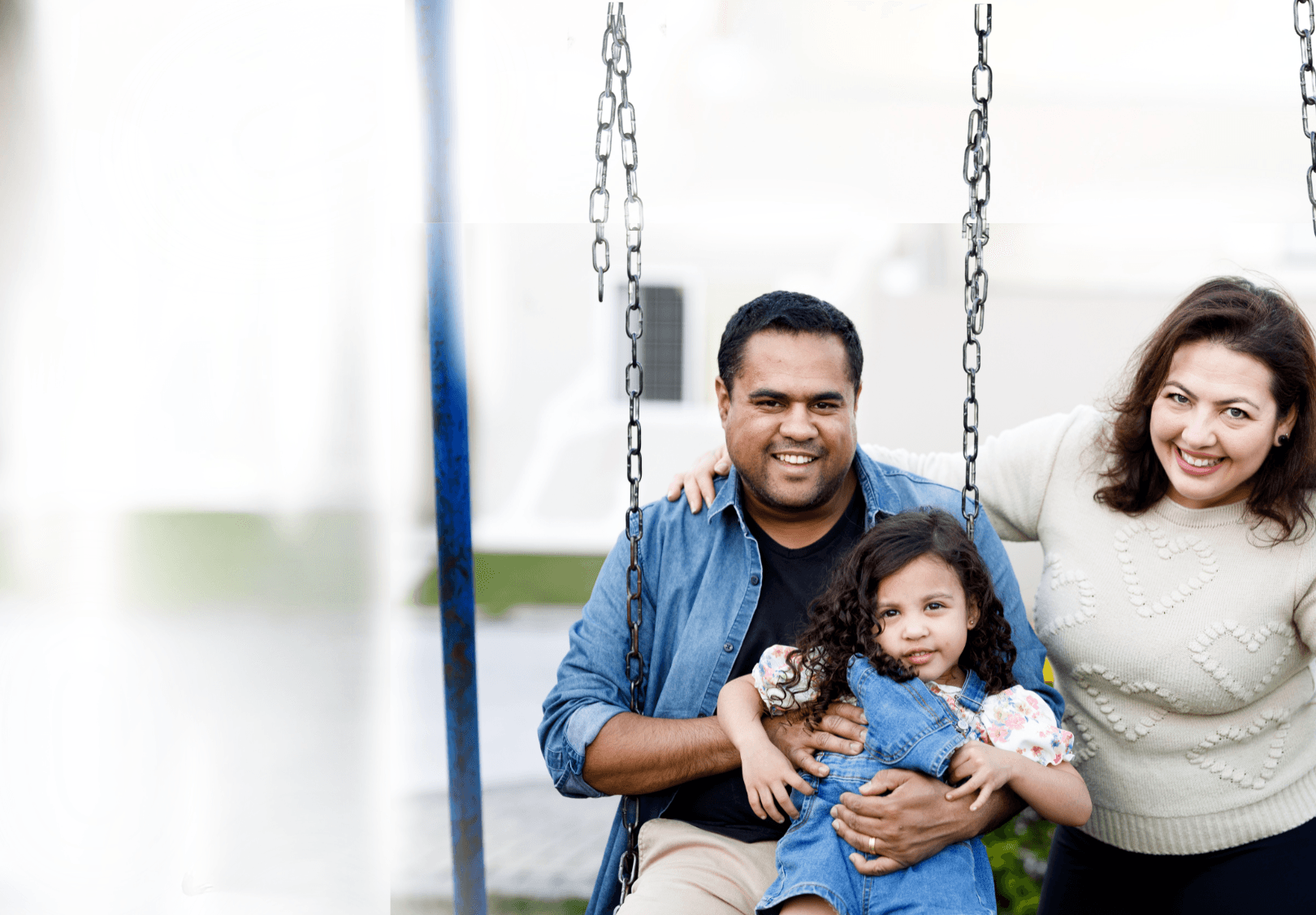 Father, daughter, and mother sitting on swings in brightly lit playground setting