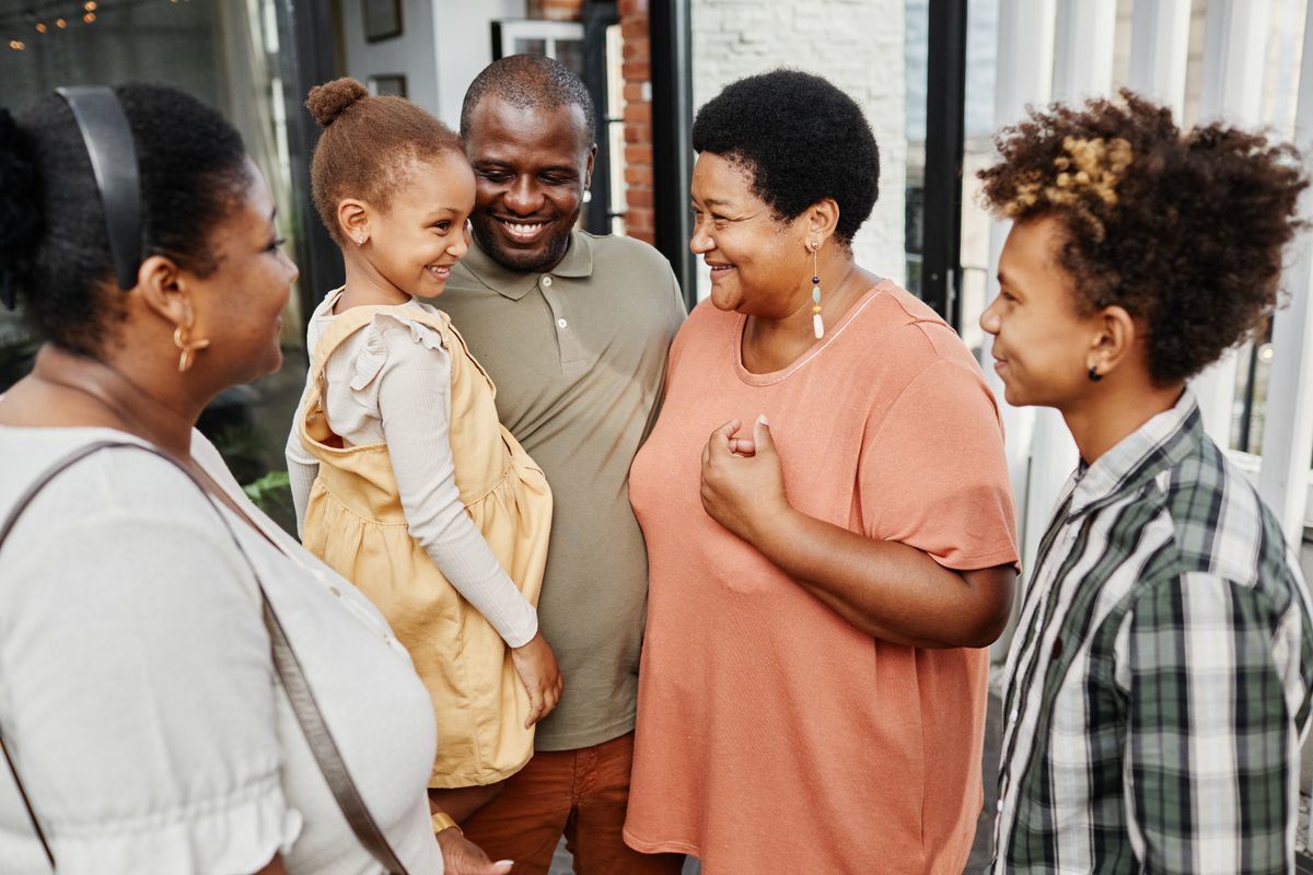 A multi-generatioinal black family smiling and looking at each other.
