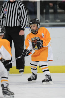 This is a picture of Jack (the blogger's son) playing hockey. He's holding his hockey stick out in front of him and wearing an orange uniform.