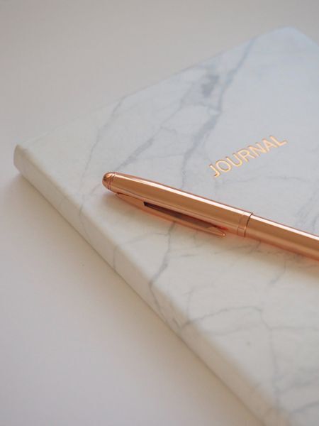 Photo of a closed journal with a rose gold colored pen laying a top the journal.