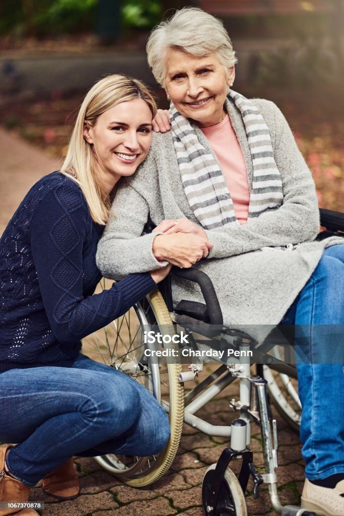 Woman on left and woman in wheelchair on right holding hands