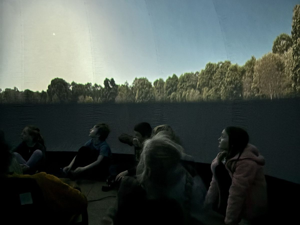Students seated inside the planetarium looking up at the night sky constellations.