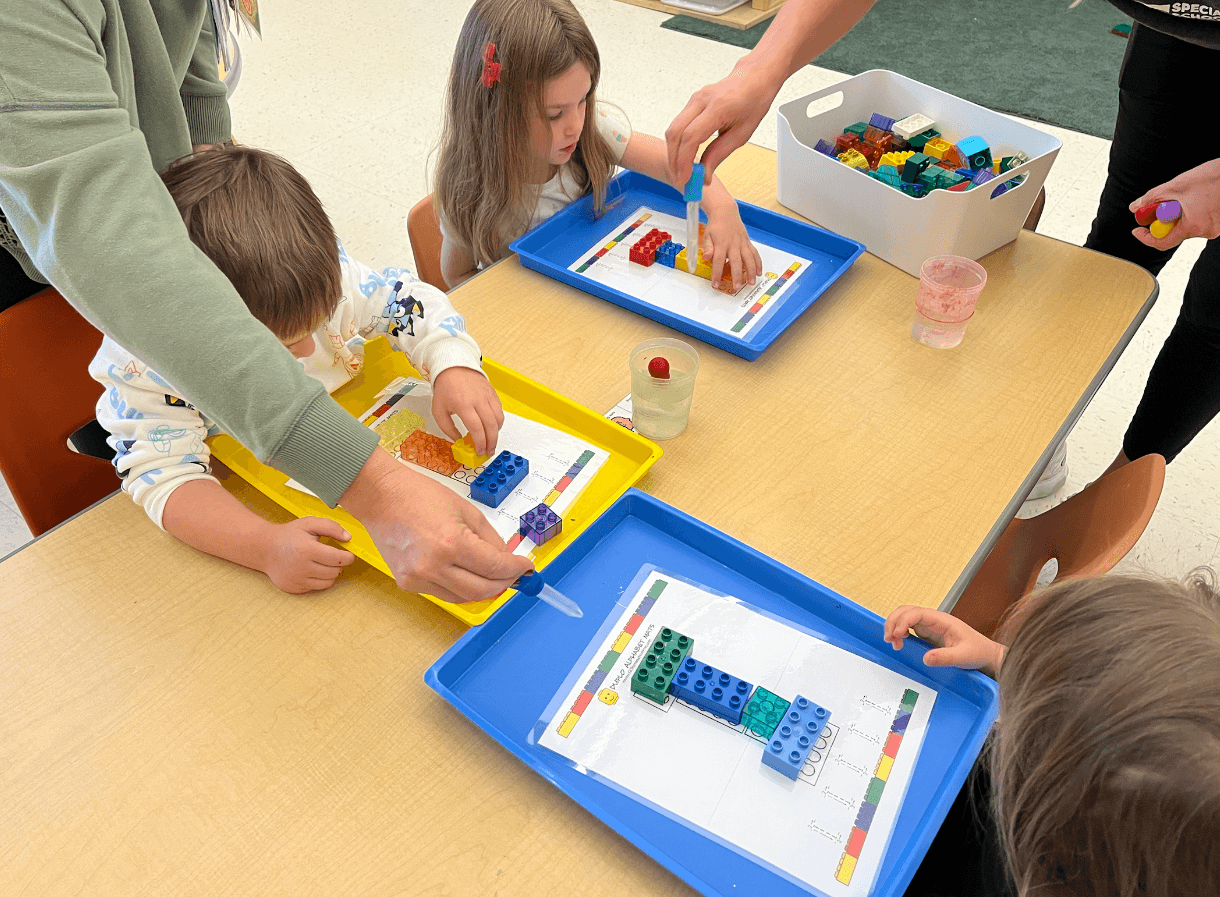 kids sitting at a table using building blocks to make letters