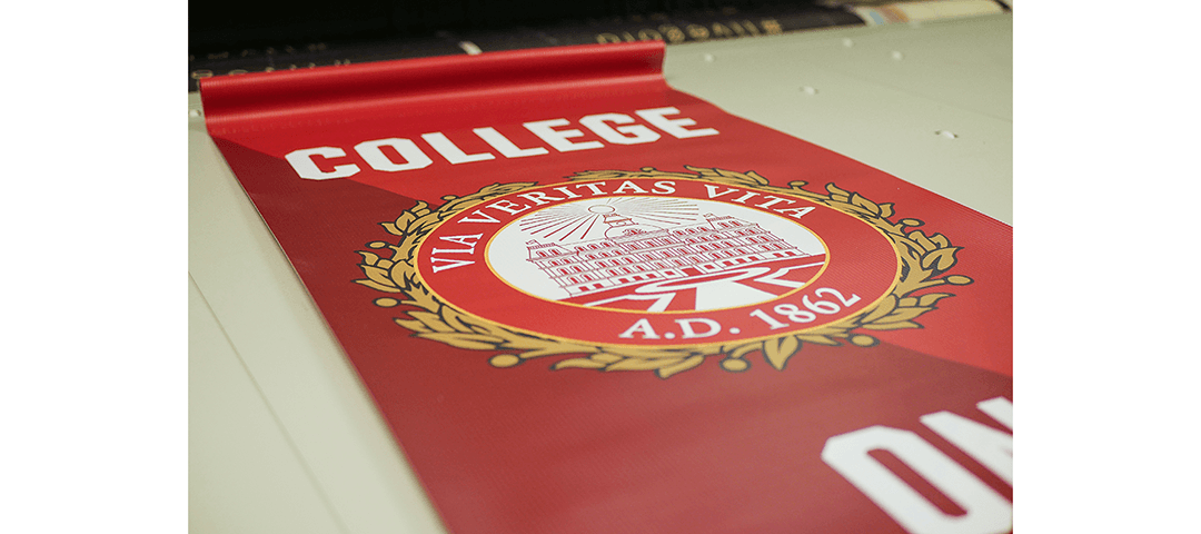 Large format printed vertical pole banner showing College on the Hill text and seal on red background