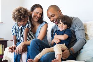 Mother and father holding hands behind a young boy and girl. Sitting in the grass