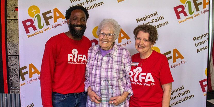 Three people standing in front of a RIFA backdrop, with one holding an award.