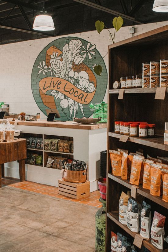 Instagrammable space in a local market featuring a "Live Local" circular mural with botanical illustrations behind the checkout counter.