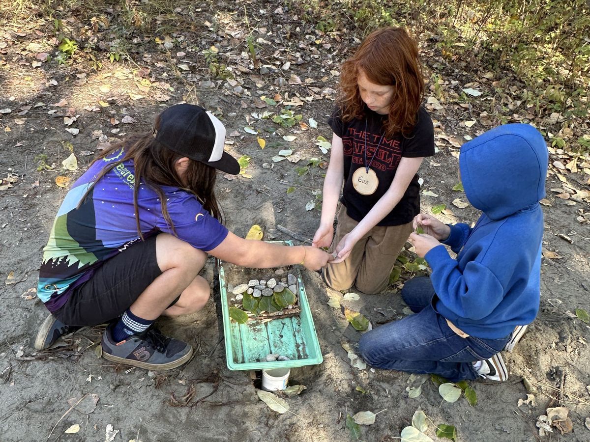 Three students leaning over a container in the sand doing an erosion activity to learn about how to create solutions for erosion.
