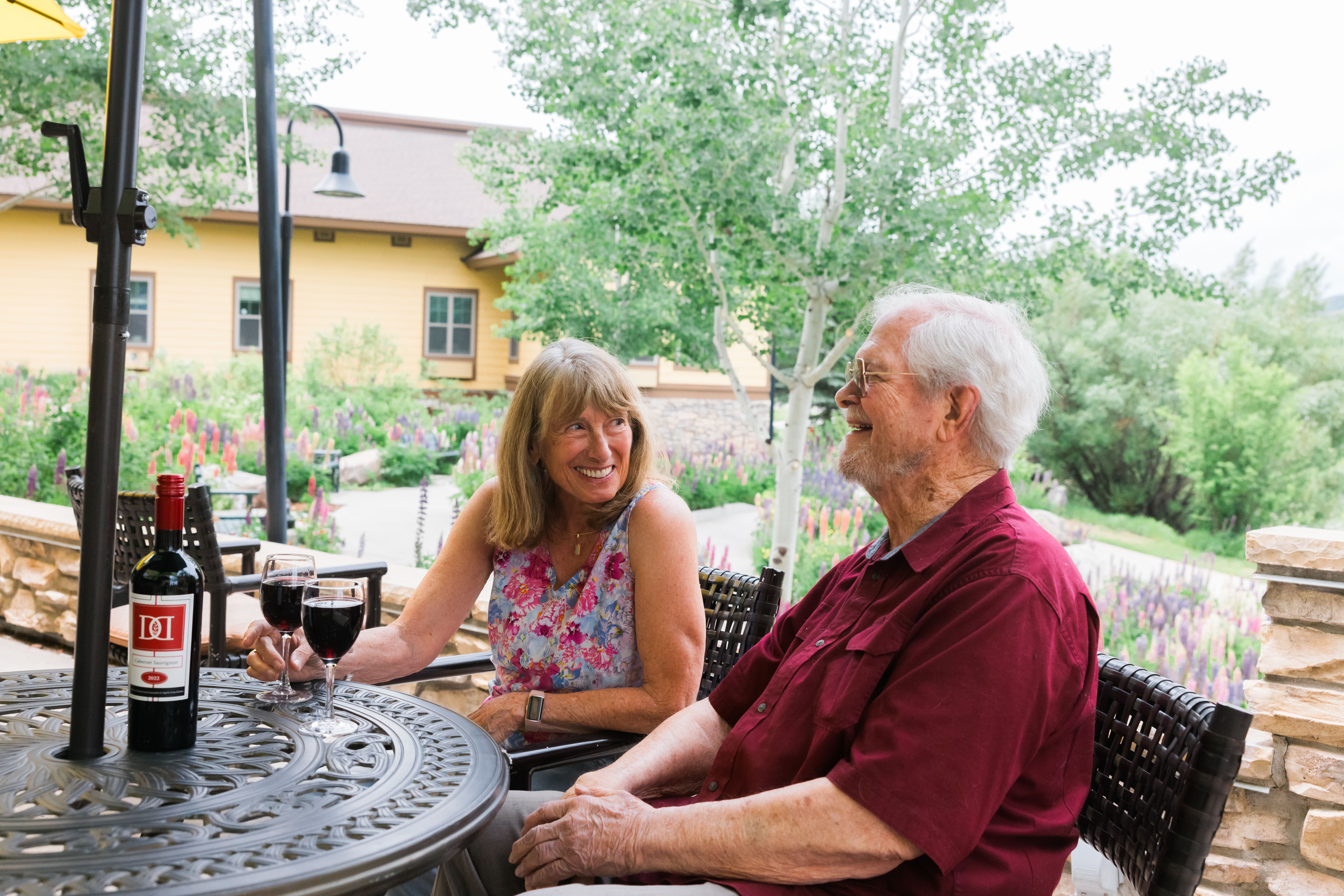 Two older adults smiling and enjoying wine on the patio of Casey's Pond Senior Living Community in Steamboat Springs, CO