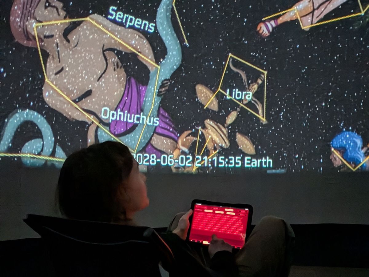 Field Educator, Jack, holding the controls inside the planetarium which is displaying constellations and zodiac.