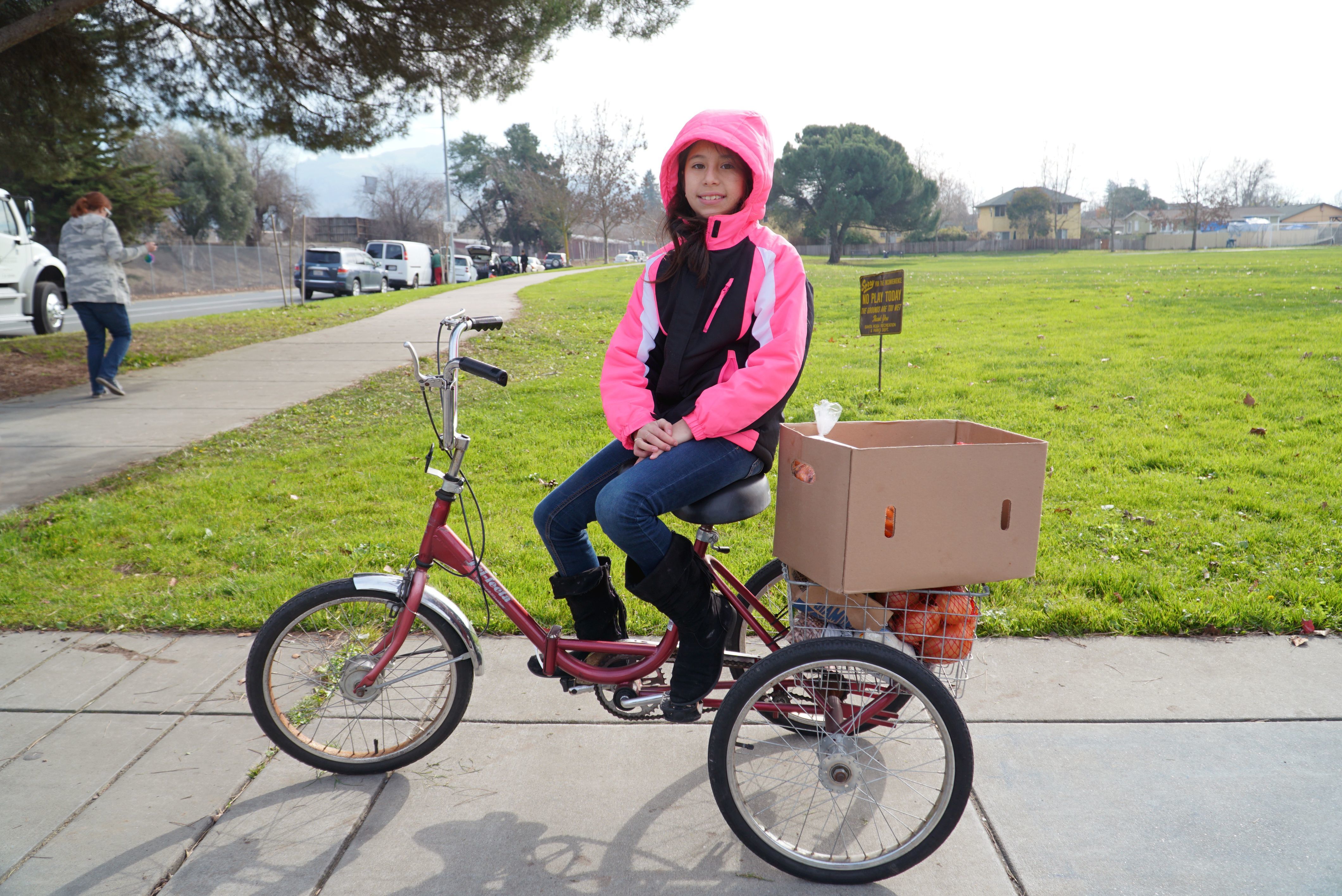 Young girl on her bicycle with a box on the back to hold groceries from the food bank