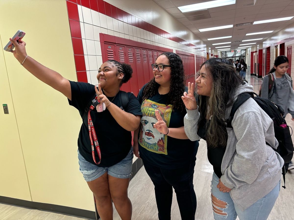 three high school girls taking a selfie in front of red lockers