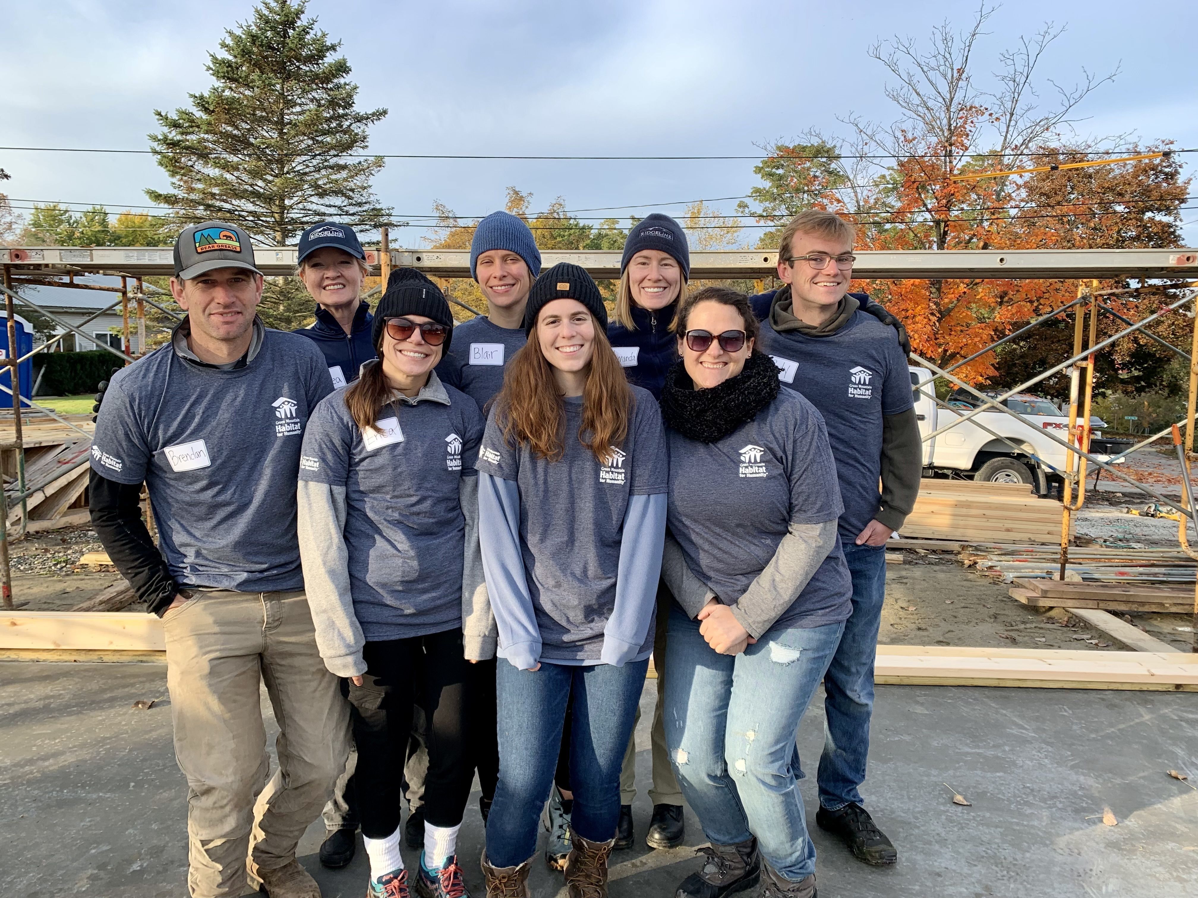 Volunteers stand in front of house under construction.