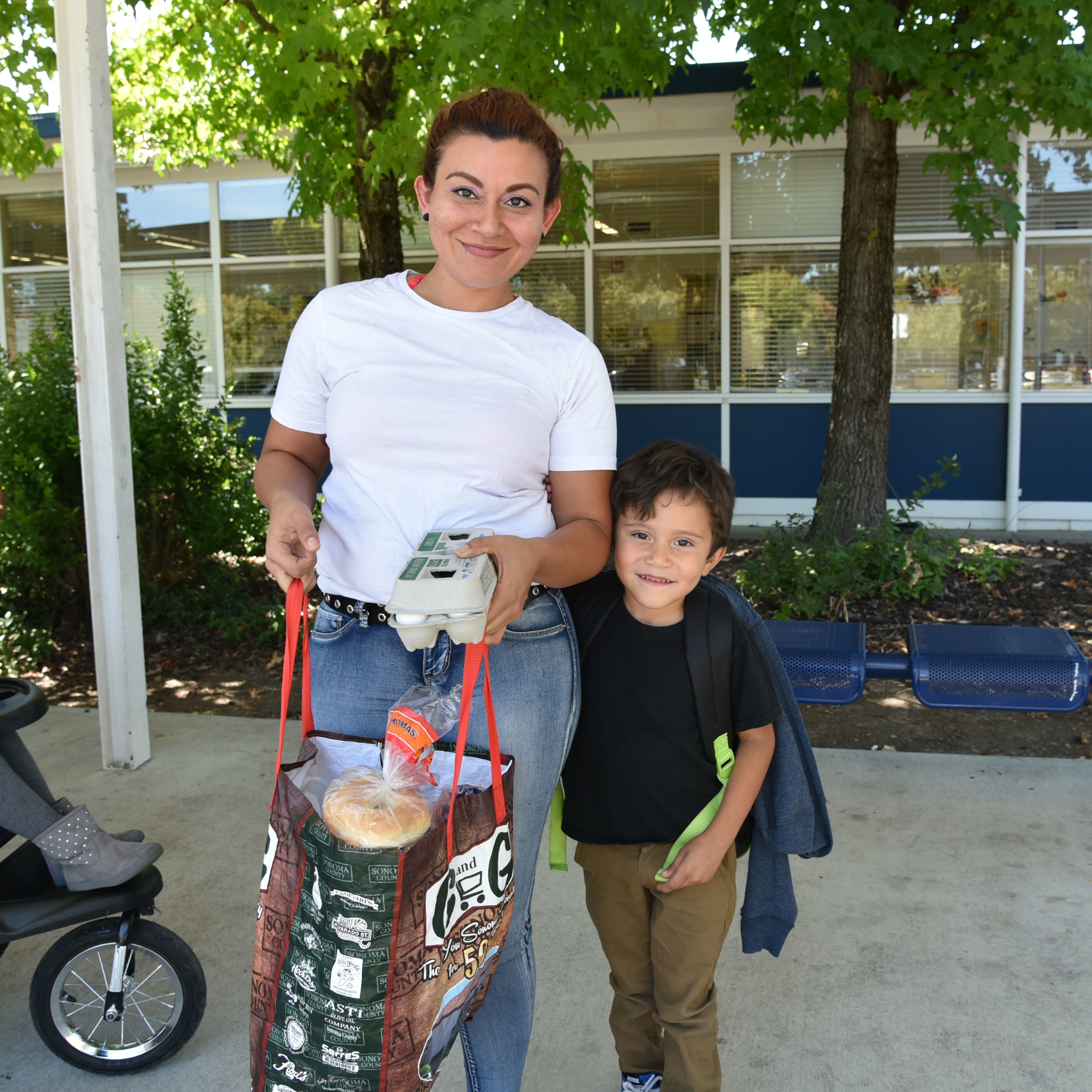 Mother with her son, smiling and holding a bag of groceries in front of a school