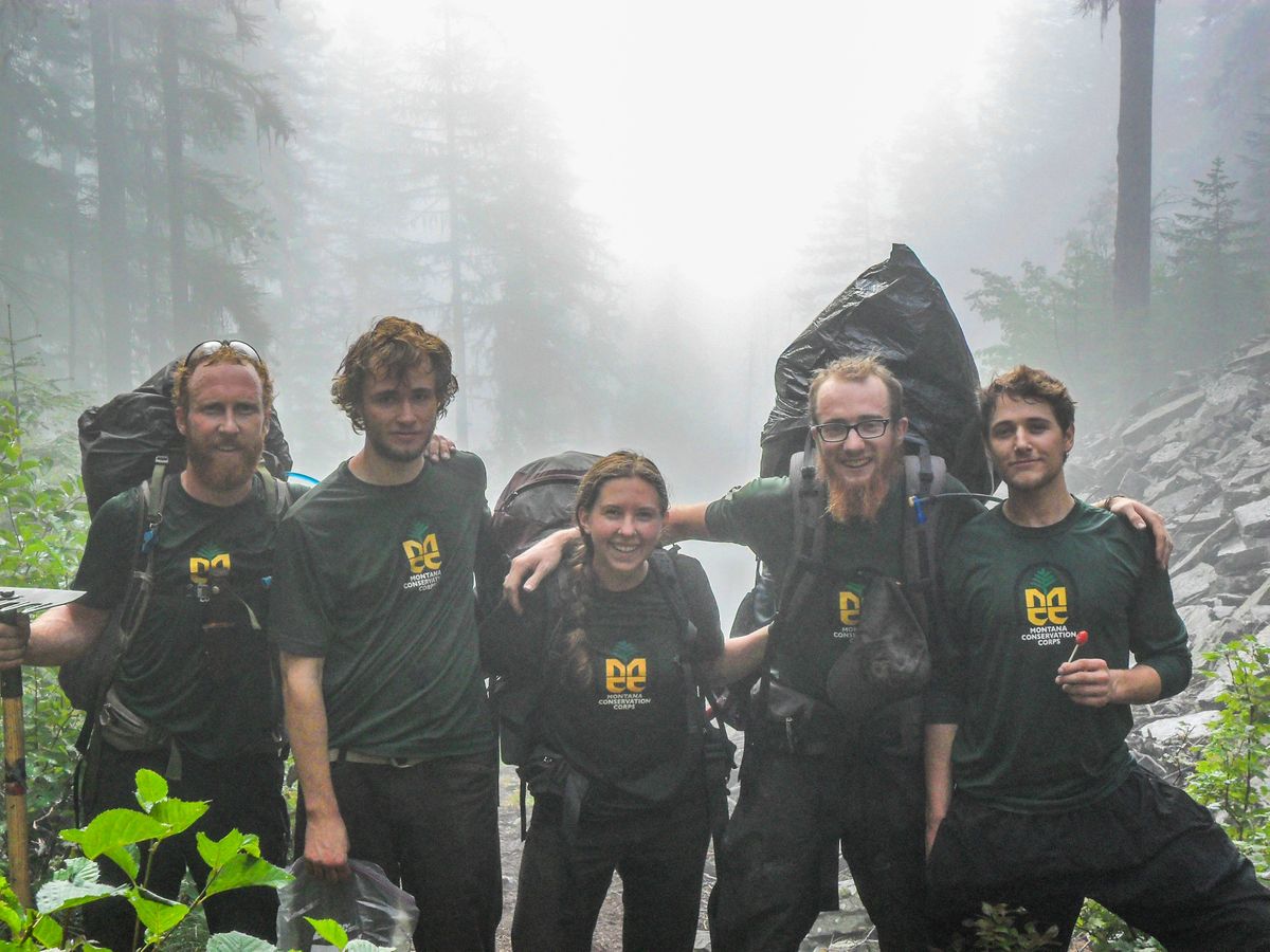 [Image Description: Five MCC Crew members stand arm in arm in a foggy gulch, surrounded by foliage.]