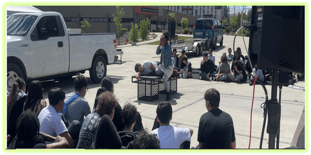 Students from Performing Arts on Broadway (PASB) present a Shakespeare in the Park performance made possible through a Marchi Mini Grant, with classmates gathered outdoors to watch.
