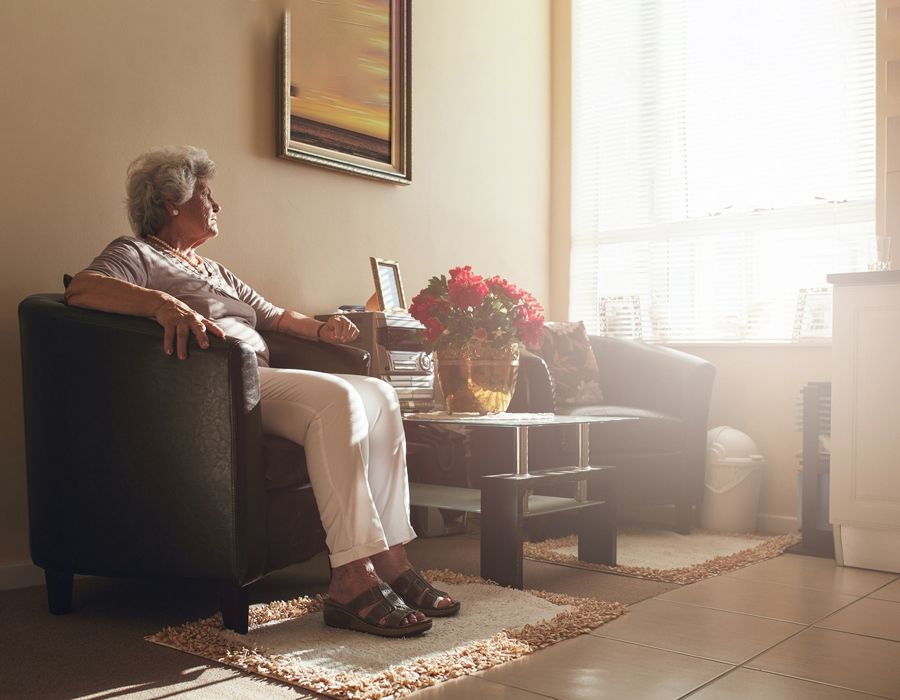 Older woman sitting isolated in her home, looking out the window solemnly