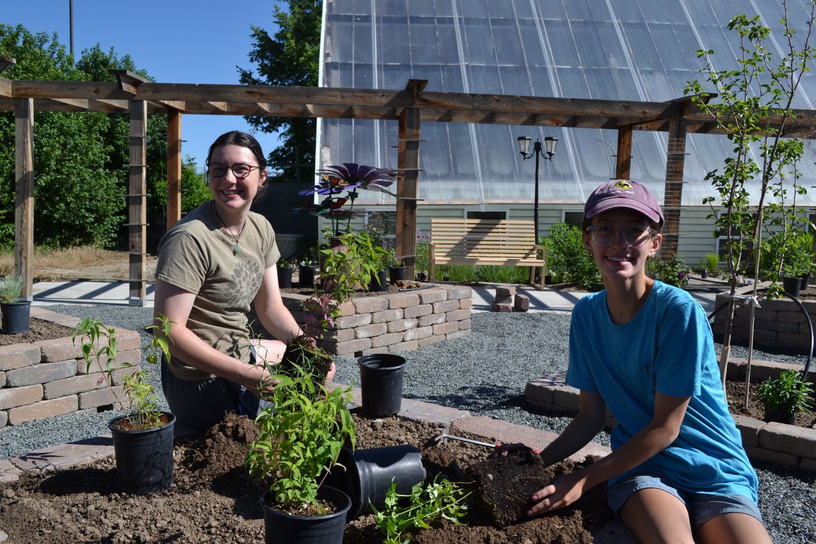 Two young women plant perennials in a raised bed.