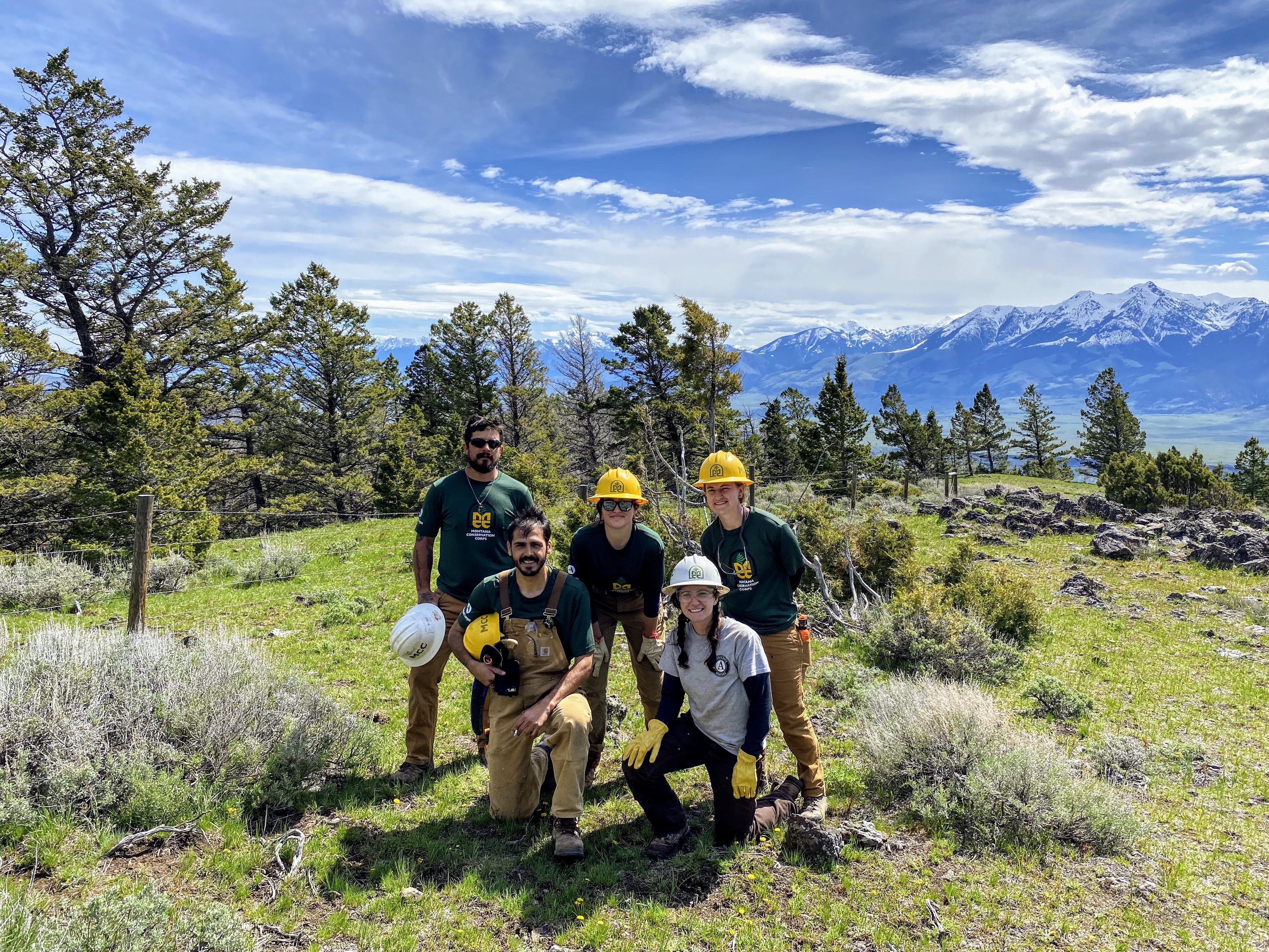 A crew stands and kneels in front of a wildlife friendly fence that they have just built.