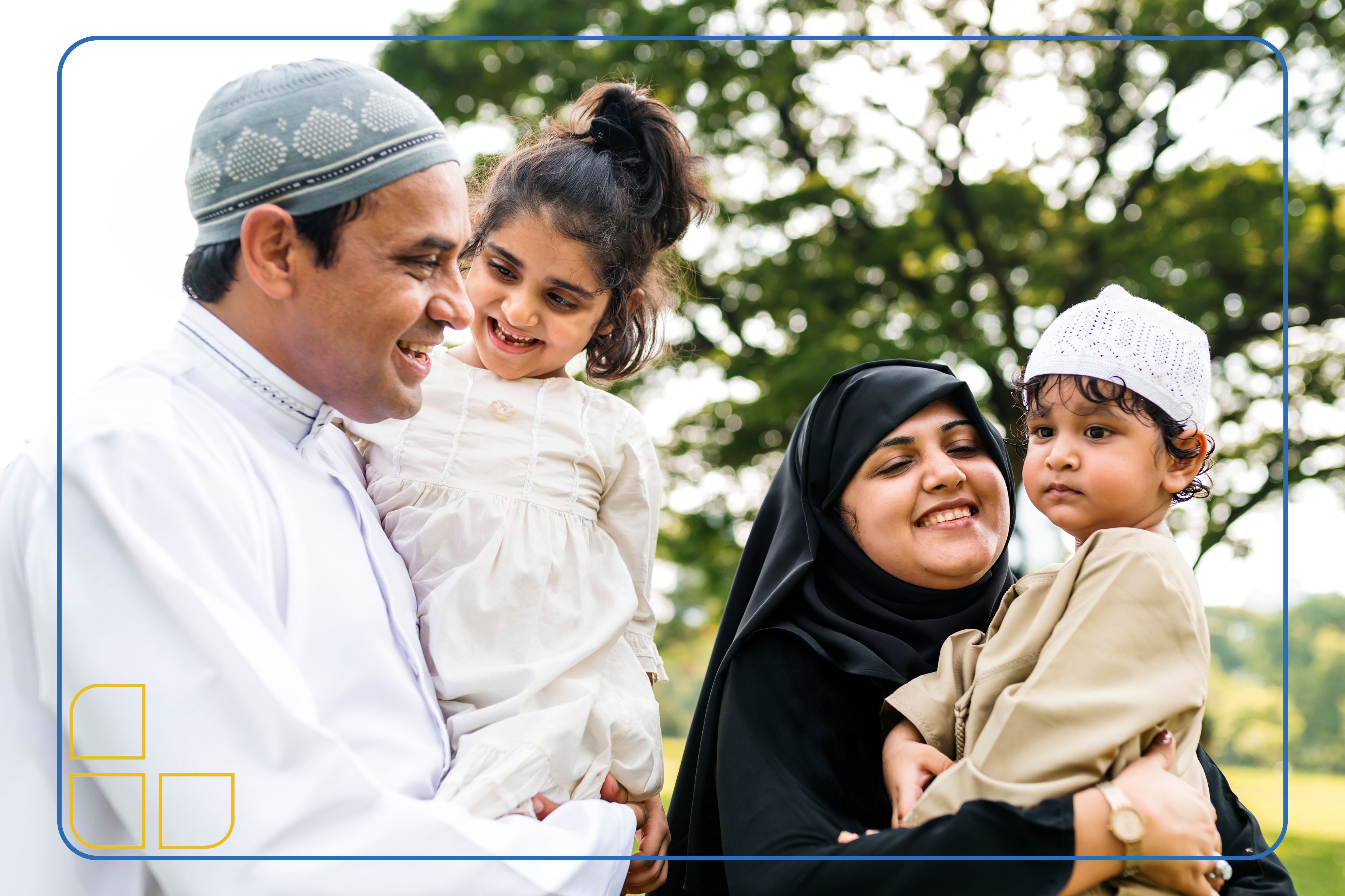 Afghan mother and father laughing and smiling together with their two children, a little boy and a young girl. The family is outdoors with a sunny background of trees. 