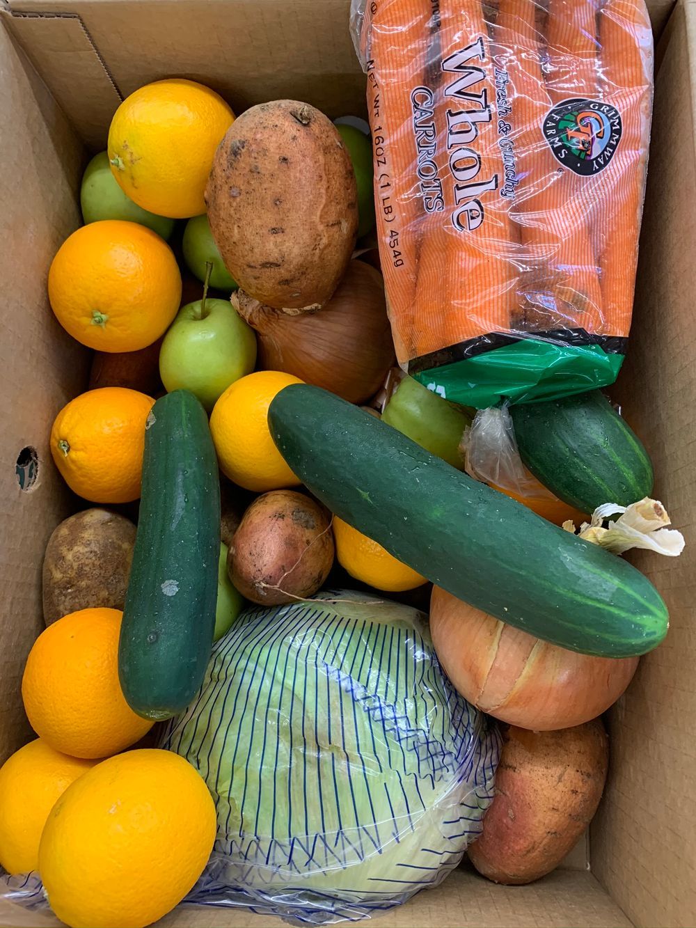A crate of vegetables and fruits is shown, including cucumbers, oranges, pears, potatoes and carrots.