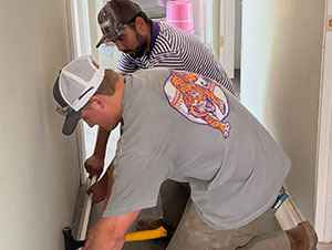 Two volunteers working together to install baseboard trim
