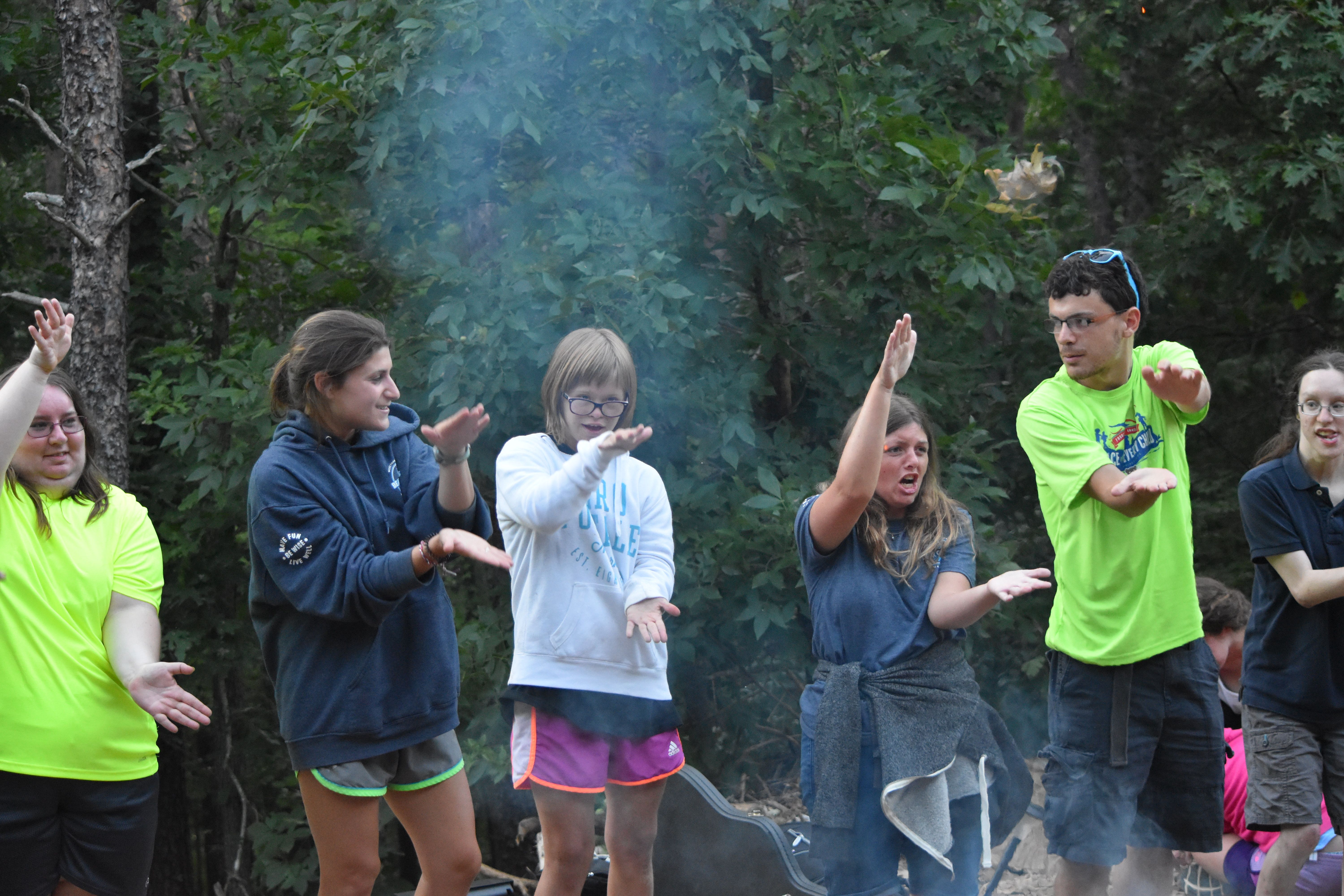 Campers and counselors sing songs by a campfire.