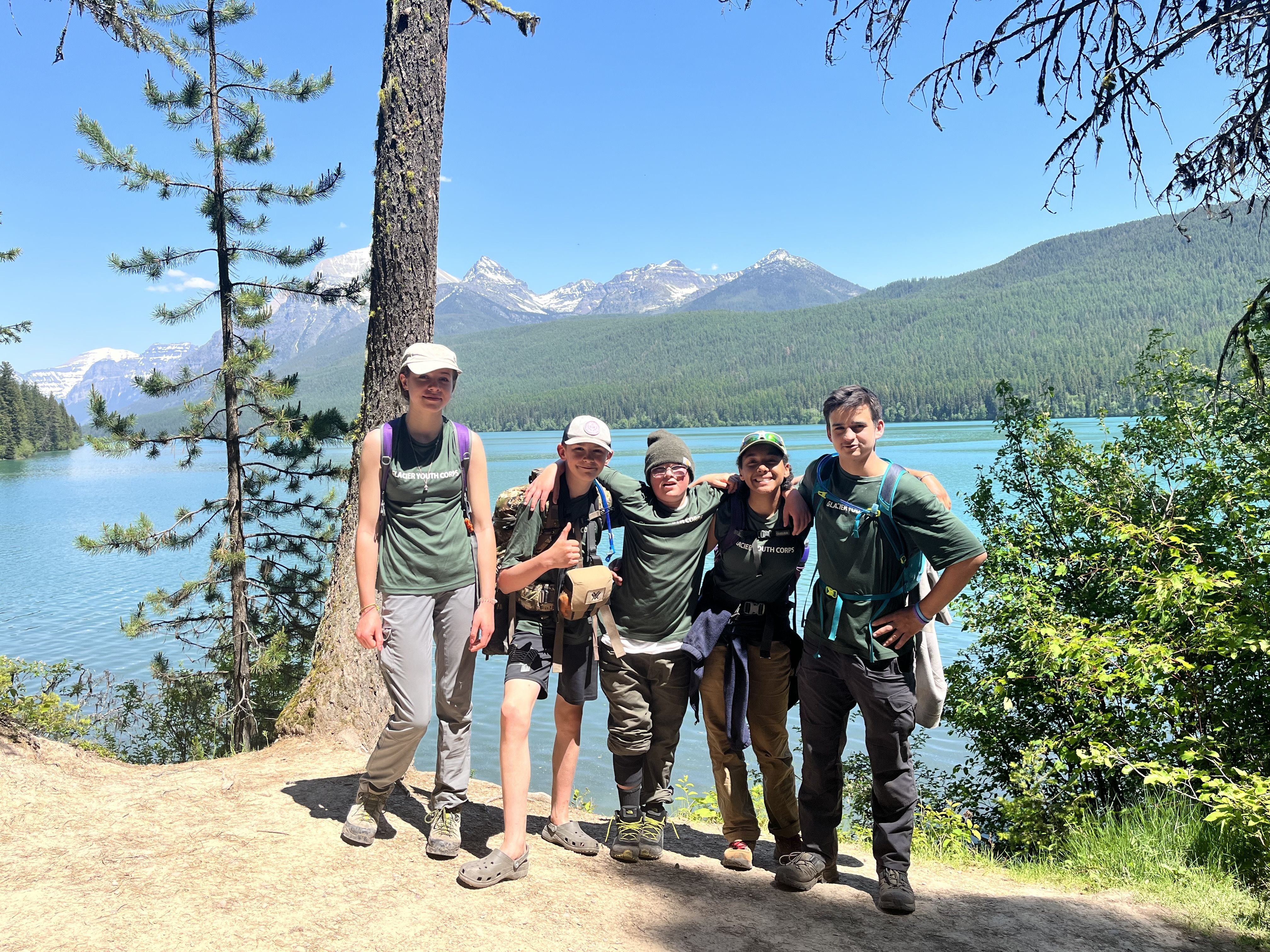 [Image Description: Two MCC members are wading into a bright blue lake. They are both wearing their MCC shirts and waders, holding nets for specimen collection.]