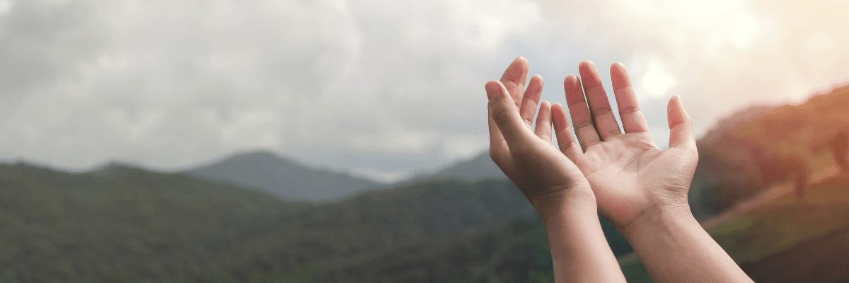 a pair of cupped hands raised to the sky with mountains in the background 