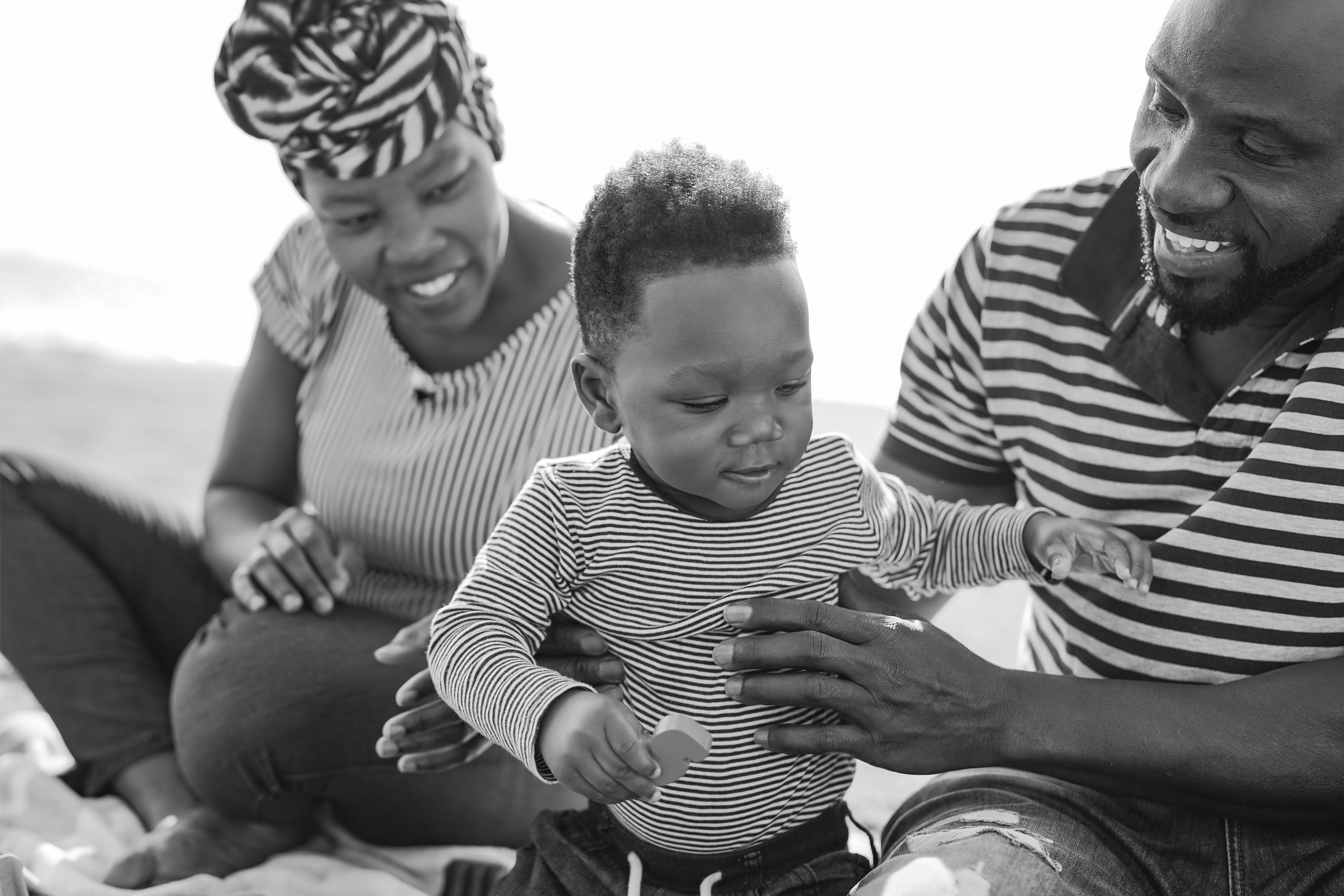 Two parents are laughing holding their smiling toddler. The image is in black and white.