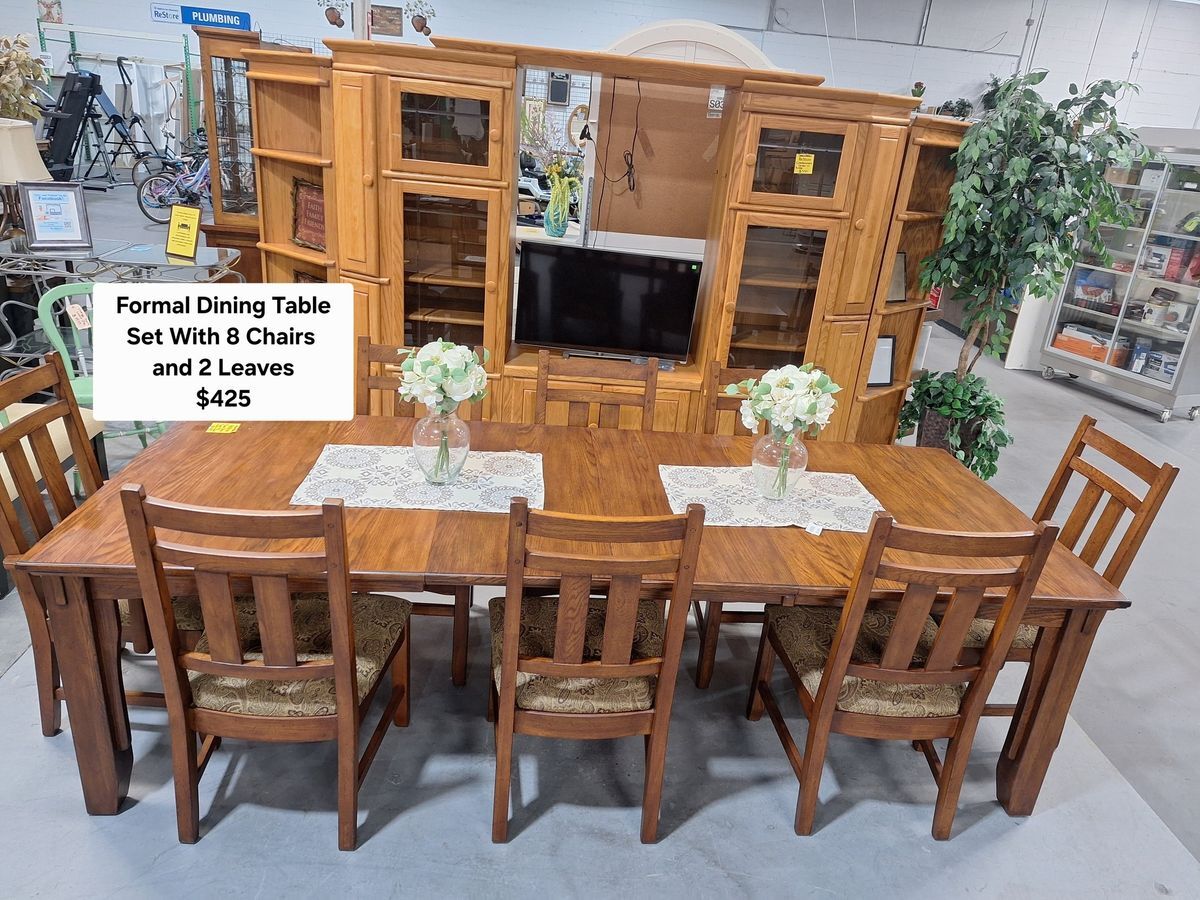 Solid wood formal dining table with eight matching upholstered chairs, floral centerpieces, and decorative runners – $425 at Habitat ReStore Zephyrhills