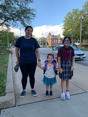 Mother holding her children's hands as they walk to school.