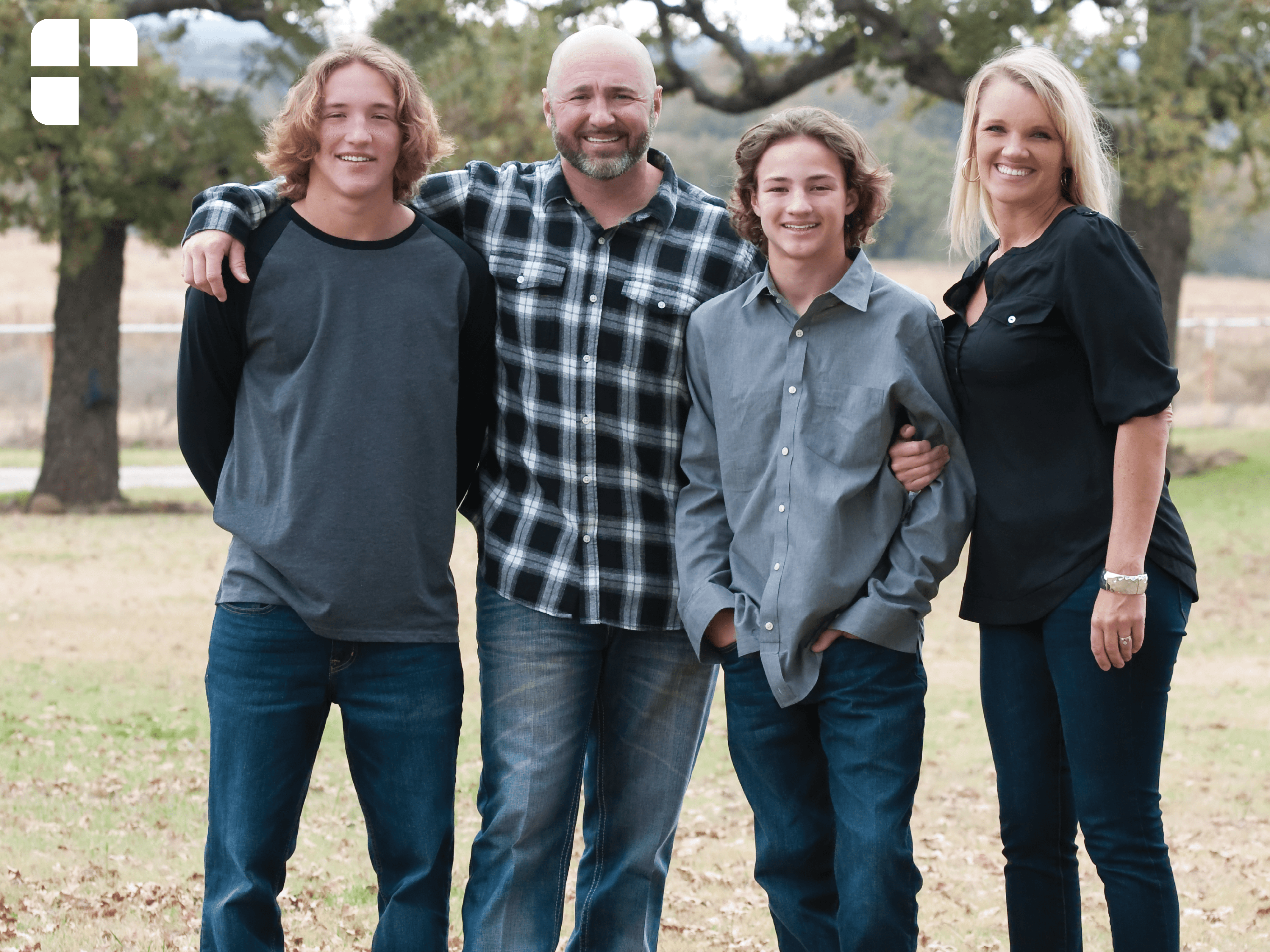 A mother, father and two sons with their arms around each other at a park.