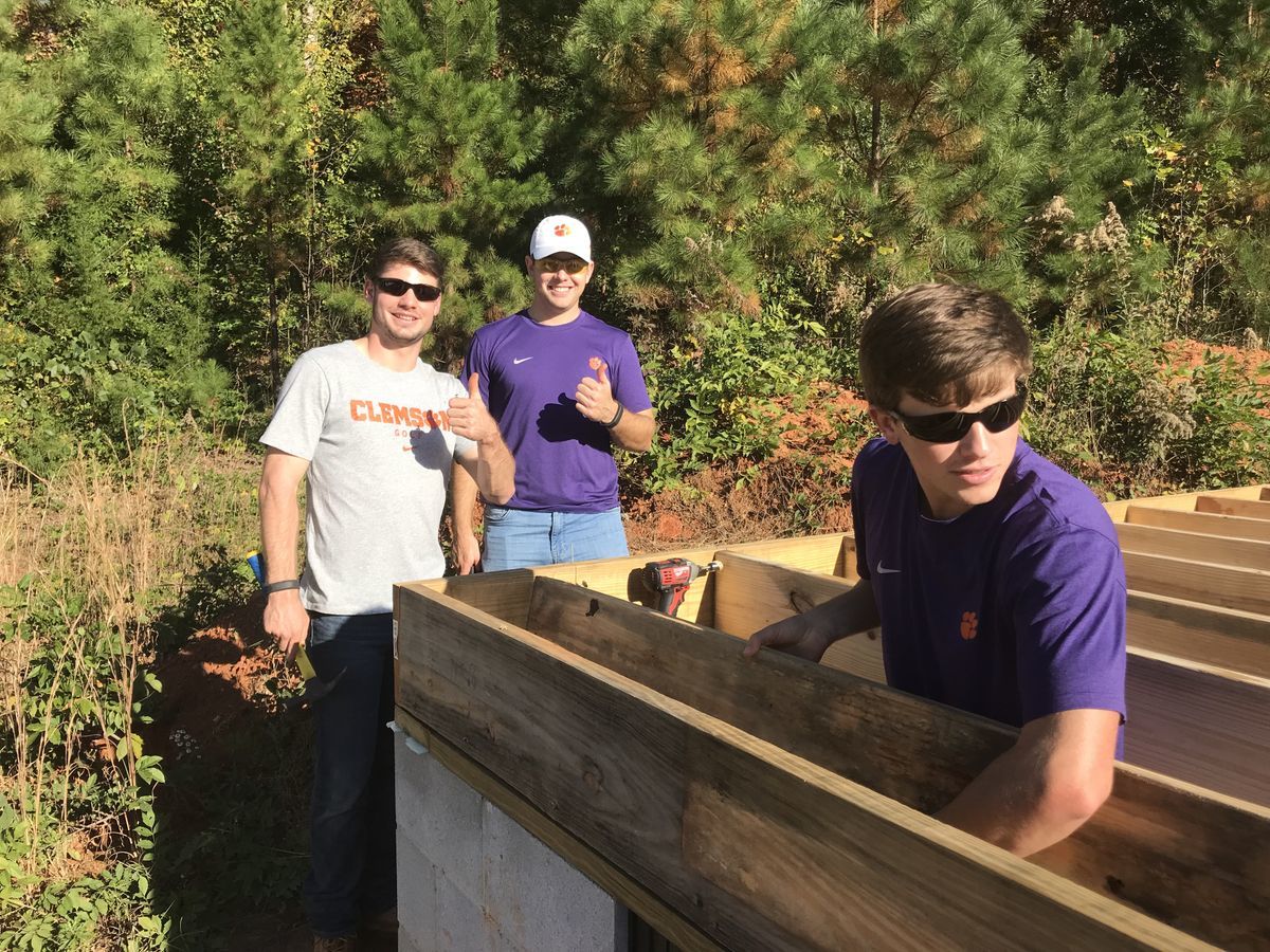 Three male student-athletes work together in the floor joists of the home. 