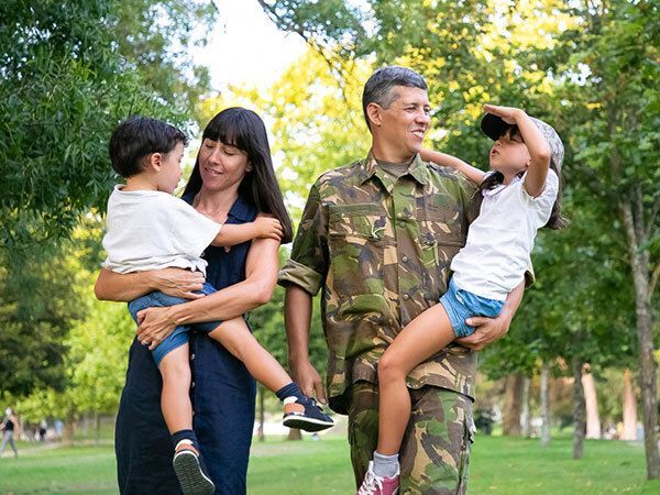 A woman and man in military attire holding two children in a park.