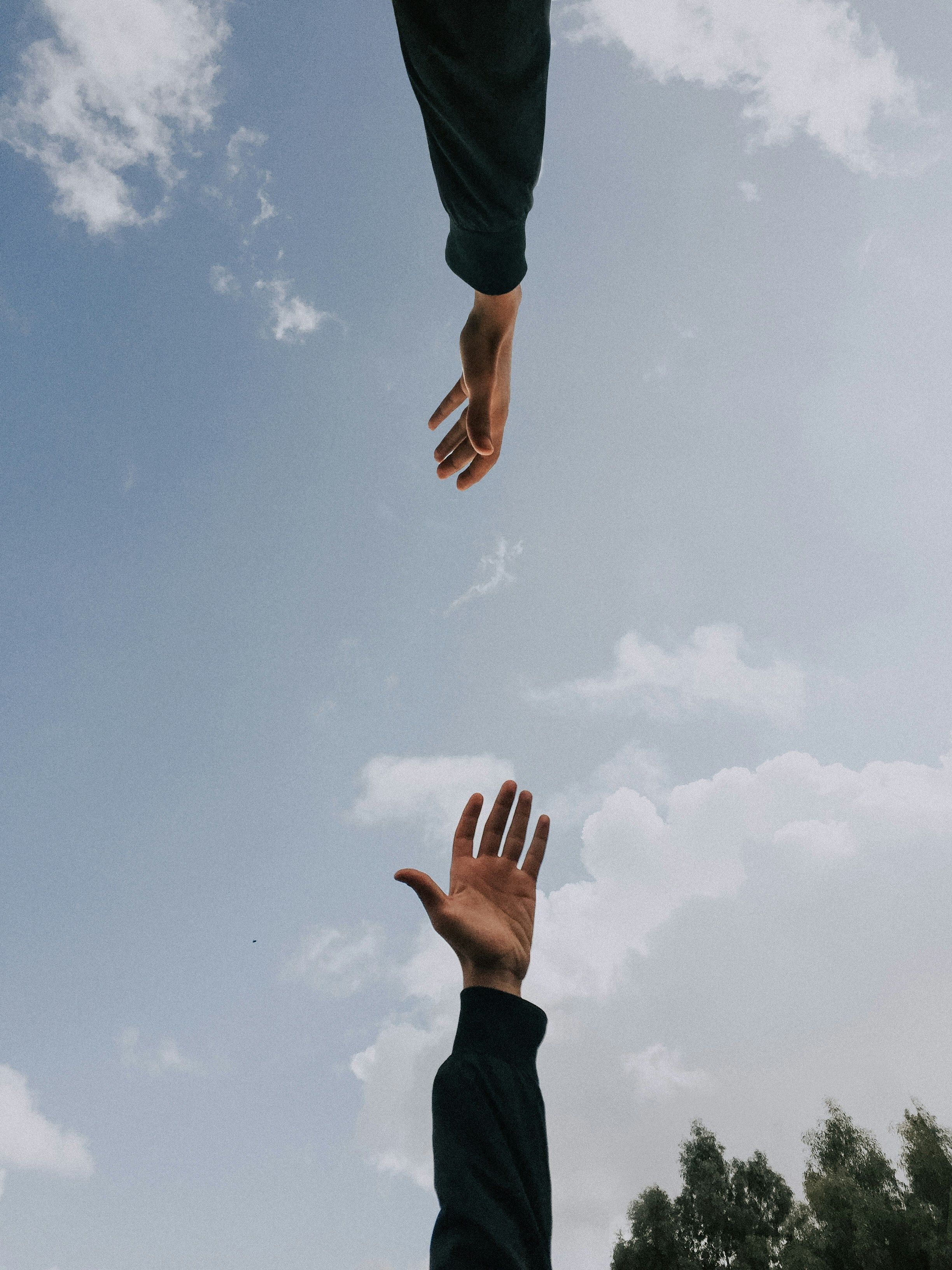 Hands reaching towards each other with the sky as a background