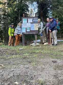 A crew stands smiling next to a trailhead sign.
