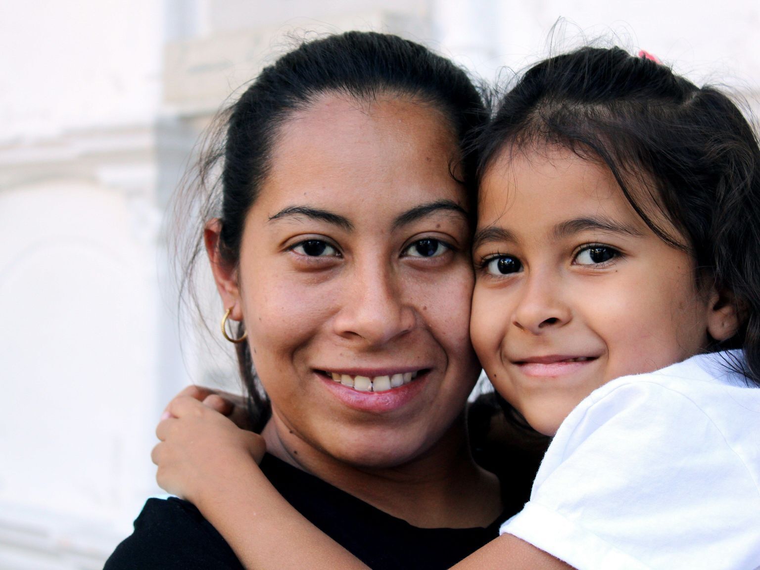 Hispanic mom holding her young daughter, both looking directly at the camera