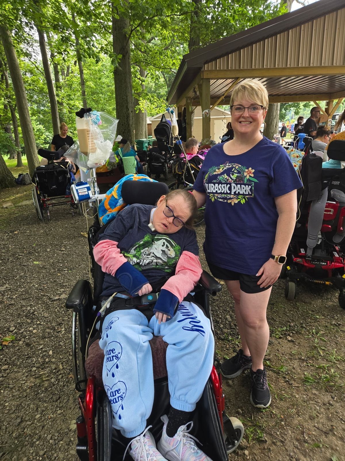 A woman with dark hair and a black jacket with a stethoscope around her neck is in the background kneeling by a man in the foreground who wears a green polo shirt. She is smiling toward him.