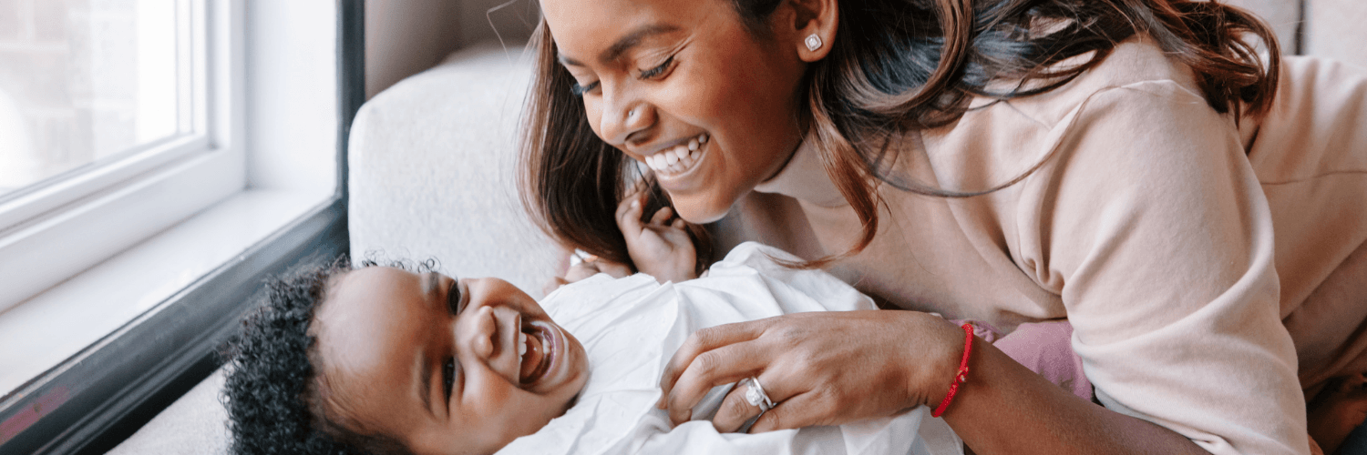 Photo of a mother smiling leaning over a smiling baby