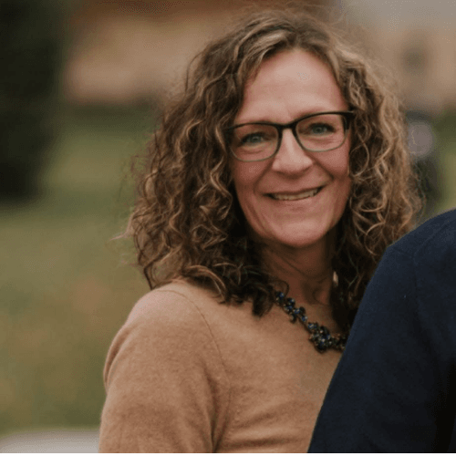 Liza smiling in a tan sweater and blurred outdoor background