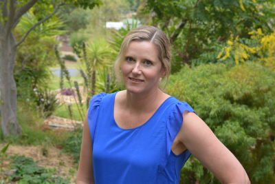 Photo of Kate Morrell smiling in a bright blue shirt with green landscape behind her.