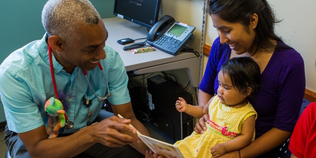 Pediatrician, baby, and mother look at book together