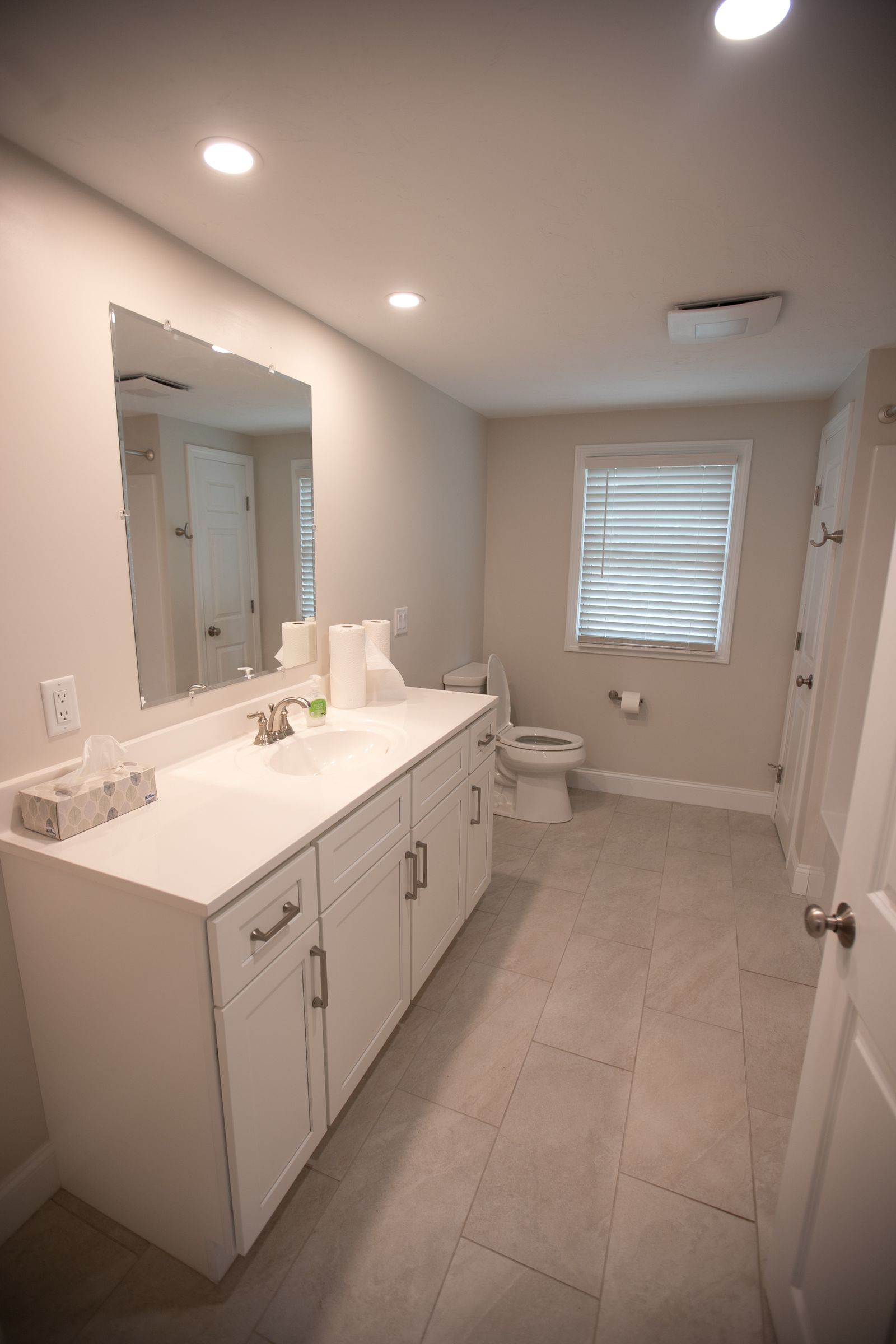 A photo showing a completed bathroom with white vanity and grey tile floors