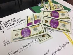  a pile of money with a purple label in the center of them, laying on top of a large check