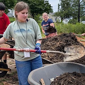 Volunteer raking mulch along the side of a house