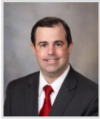 Photo of Dr. John Eaton wearing a red tie, black suit, and smiling at the camera