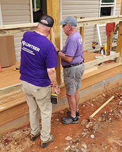 Five Purple Heart Homes volunteers in purple shirts posing together outside a house under construction