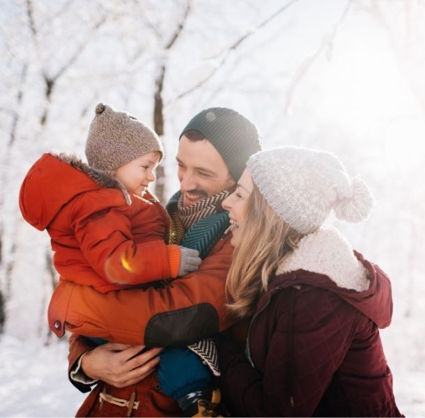 Parents looking at their young son and smiling. They are all in winter gear and outside.
